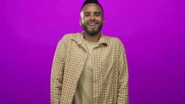 Stüdyoda mor arkaplana karşı ekose gömlek giyen, yüzü ve sakalı görünen Latin asıllı genç bir adam..