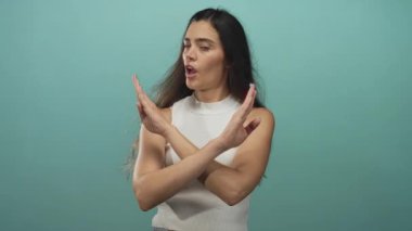 Kadın stüdyo duvarına karşı kollarını kavuşturuyor beyaz kolsuz bluzuyla ciddi bir ifadeyle; reddedilme meydan okuması.