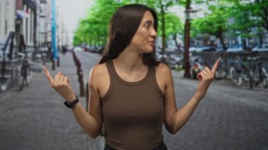 İspanyol kadın, kaldırım taşı sokağında orta parmaklarını görünür ellerle ve kahverengi kolsuz tişörtle gösteriyor..