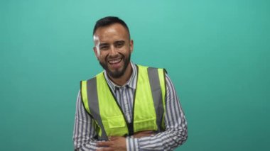 Yansıtıcı güvenlik yeleği ve çizgili tişört giyen genç adam stüdyo da kapalı ellerle gülüyor..
