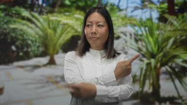 Çapraz kollu bir kadın, yeşil bitkilerin arasına yerleştirilmiş ormanda işaret ve açık avuç içlerini işaret ediyor; belirsizlik..