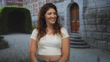 Çıplak göbek ve inci kolyeyle gülümseyen bir kadın şehrin girişinin önünde duruyor. Kendine güveni tam..