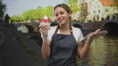 Amsterdam caddesinde elinde çilekli ve kremalı bir tatlı bardağı tutan kadın kot önlük ve plastik eldiven giyiyor..