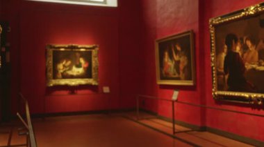 Kırmızı galeri duvarları ve yumuşak bokeh çerçeveli resimlerle bulanık müze içi; arkaplan telif alanı sakinliği.