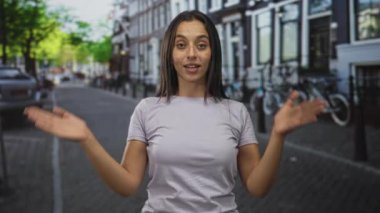 Elleri havada ve avuçları görünen İspanyol bir kadın parktaşı şehir sokağında park halindeki bisiklet ve kanal evlerinin yanında duruyor..