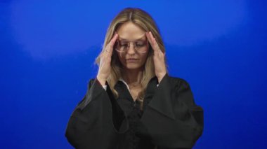 Kadının elleri, stüdyo görüntüsünde mavi izole arkaplanda genç sarışın yargıç üniforması figürünü gösteriyor..