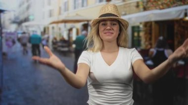 Kadın, dışarıdaki kafenin yanındaki kaldırım taşlı terasta elleri olan hasır şapkayı düzeltiyor; yaz tatili neşesi.