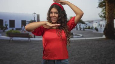 Çıplak omuzlu İspanyol kadın ve elleri kıvırcık saçlı çerçeve, sokakta kırmızı bluz ve kot pantolon içinde gülümseyen;.