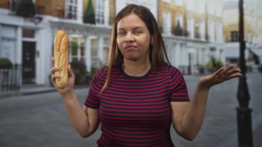 Sol el kaldırılmış baget tutan ve çizgili gömlek ve büzüşmüş dudaklar giyerken çimdiklenmiş parmaklar hareketi yapan kadın; açlık sıkıntısı.