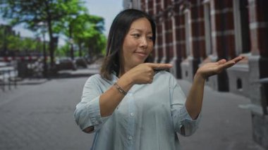 Kadın, gülümseyen ve eline bakan şehir caddesinde avucunu açmak için parmağını işaret ediyor; dostça bir davet.