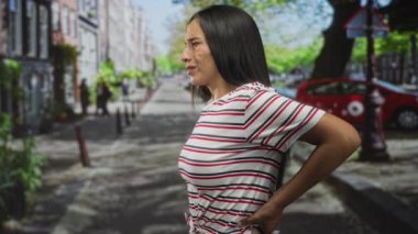 Sokakta sırtı ağrıyan bir kadın, park halindeki araba ve kürek çekilen evlerin yanında yaralı bir yüzle sırt ağrısı çekiyor..