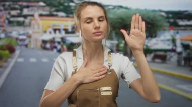 Şehir sokaklarında jest yapan kadın, önlük giyiyor, samimiyet ve ifade sergiliyor, açık şehir manzarası ile çevrili..