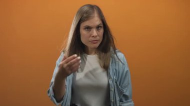 Kadın saç tellerini ayarlar ve stüdyoda turuncu bir arka plana karşı omuz üzerinden kilitler; iç gözlem.