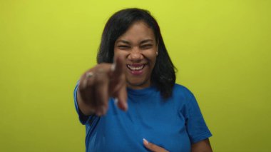 Afro-Amerikalı kadın kamerayı işaret ediyor ve limon yeşili stüdyoda geniş bir gülümseme sergiliyor; neşe dolu kahkahalar mutluluk eğlencesi.