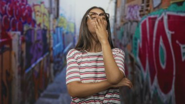 Sokak grafiti sokağında baş ağrısı, çizgili gömlek ve gözlüklü kadın; Yorgun kentsel dayanıklılık.