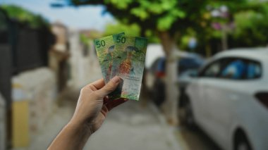 Bir şehir caddesinde İsviçre frangı banknotları tutan adam, hareketli bir ortamda kentsel mali işlemlerin ve para değişimi özünü yakalıyor..