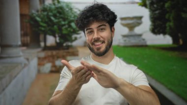 Güneşli bir günde açık havada el kol hareketi yapan sakallı genç bir adam yaz atmosferinde duygularını dışa vuruyor..