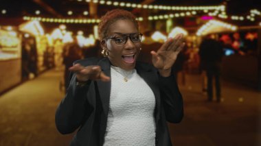 Gözlüklü ve altın küpeli bir kadın gülümsüyor ve parmakları şehir caddesindeki işlek markette renkli hediyelik eşya dükkanını işaret ediyor..