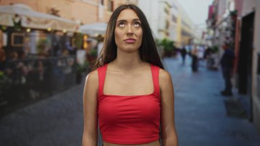 Kırmızı etek giyen, gözleri kapalı bir kadın açık hava restoranının yanındaki terasa bakıyor ve kaldırım taşı yolu; düşünceli bir yansıma..