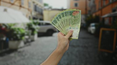 Bir şehir caddesinde elinde Arjantin pezosu olan bir adam açık havada şehir geçmişi bulanık ve mali ve ekonomik bağlamda belirgin bir şekilde gösterilen beyaz eli olan banknotları gösteriyor..