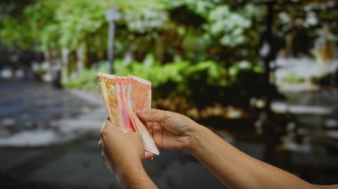 Açık şehir ortamında Filipinli pezoları tutan eller, canlı şehir manzarası arka planında iş ve yatırımı simgeliyor.