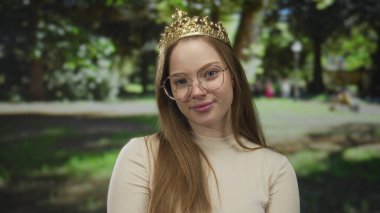 Altın taç takan ve ince gözlükler takan Kafkas Prensesi, açık bir ormanda, bulanık yeşil yapraklar arasında çapraz kollarıyla duruyor..