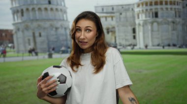 İtalya 'da Pisa Tower' da elinde futbol topu tutan bir kadın gün içinde canlı bir arka plana karşı neşeli bir ifade sergiliyor.