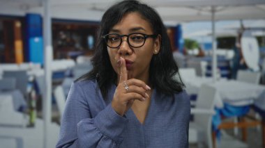 Kadın sessiz kalmak için parmaklarını açık restoran terasında boş masaların yanına büyük beyaz şemsiye altına koyar..