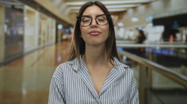 Çizgili tişörtlü gözlüklü kadın başını arkaya eğiyor ve mağaza koridorunun içinde gözlerini kapatıyor; huzur yansıması.