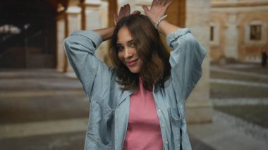 Eski bir üniversite binasında neşeli jestler yapan bir kadın gençlik ruhunu ve İspanyol mirasını tarihsel bir zemine karşı sergiliyor..