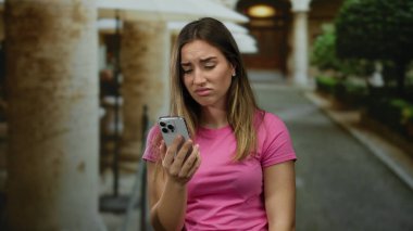 Lokantadaki terasta oturan bir kadın endişeli bir ifadeyle akıllı telefonuna bakar. Çevresi sokak havasıyla çevrilidir. Sıradan ve kentsel bir yaşam tarzını vurgular..