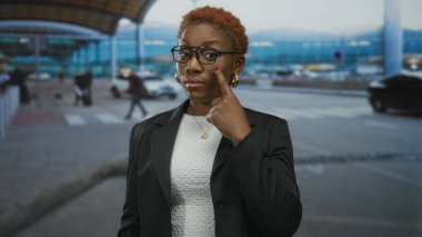 Genç Afro-Amerikalı bir kadın gölgelik altındaki yoğun bir havaalanı terminalini işaret ediyor..