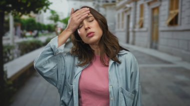 Kot giymiş bir kadın, şehir içinde sokakta başını tutuyor ve şehir ortamında genç İspanyol ifadelerinin yakalanması sırasında strese girildiğini söylüyor..