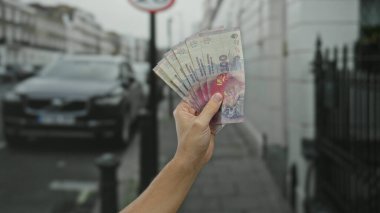 Şehir caddesinde erkek eli Arjantinli pezoları tutuyor, arabaların ve kentsel çevrenin bulanık geçmişiyle finansal temayı yakalıyor, parayı ve ekonomik sembolizmi vurguluyor..