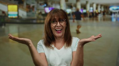 Havaalanı terminalinde gülümseyen bir kadın, hareketli gezginlerle çevrili, hareketli insanlarla dolu, hareketli bir ev ortamında neşe ve heyecanı somutlaştıran, seyahat beklentilerini yansıtan.