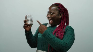 Beyaz arka plan üzerinde dolar banknotları olan bir kadın tasarruf kavramı sergiliyor ve sürpriz ve heyecan ifade ediyor.