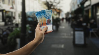 Şehir caddesinde İsviçre frangı tutan bir adam, açık hava ortamında para sergiliyor, İsviçre 'nin canlı ortamının finansal yönünü vurguluyor..