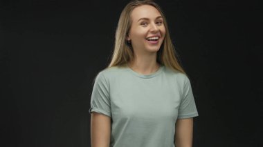 Uzun saçlı beyaz bir kadın izole edilmiş siyah arka plan duvarına karşı gülümsüyor. Günlük gömlek giyiyor. Stüdyo ortamında mutlu ve mutlu görünüyor.