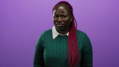 Afro-Amerikalı bir kadın cesur, mor izole bir geçmişe karşı reddedilmiş bir jestle onaylamadığını belirterek otantik duygular ve canlı moda seçimleri sergiliyor..