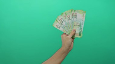 Erkek el, Rus rublesi banknotlarını canlı yeşil bir arka planda izole ederek basit ama çarpıcı bir şekilde finansal konsepti sergiliyor..