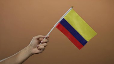 El ele tutuşan Kolombiya bayrağı kahverengi bir duvarda, izole bir arka plan, vatanseverlik ve kültürel gurur gösterisi.