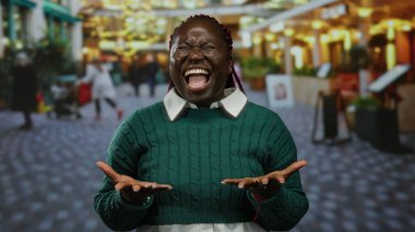 Kalabalık şehir sokak ortamında tutkuyla bağıran bir kadın, bulanık kentsel geçmişe sahip yeşil bir kazak giyiyor, hayal kırıklığını ya da öfkeyi ifade ediyor, heyecan verici duyguları canlı bir şekilde ifade ediyor..