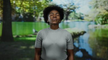 Huzurlu bir park ortamında, derin derin derin nefes alan bir kadın, yemyeşil, sakin, güneşli bir günde dinlenme ve sükuneti kucaklıyor..