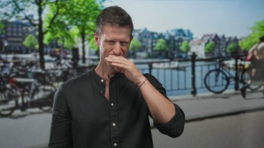 Amsterdam 'da boynunu göstererek gülümseyen ve yakası açık bir adam; kentsel sessizlik içgözlem sükuneti.