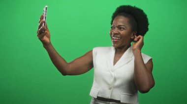 Stüdyo yeşil ekranda akıllı telefon tutan ve gülümseyen bir kadın. Neşeli bir bağlantı..