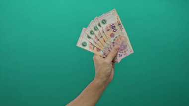 Arjantin pesolarını yeşil arka planda tutan adam, izole edilmiş elle para gösteriyor..