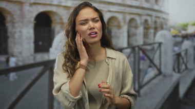 Roma 'da, sembolik kolezyumun yanında dikilen bir kadın, yanağında bir elle acıyla İtalyan çevresindeki İspanyol özelliklerini vurgulayarak, kendini rahatsız hisseder..