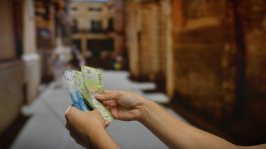 Bir şehir caddesinde Şili pesosu tutan adam şehir yatırımını ve açık havada para alışverişini resmediyor.