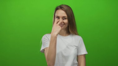 Genç beyaz kadın gülümsüyor ve neşeli bir jest yapıyor, parlak yeşil bir arka planda, neşeli ve neşeli bir sahne yaratıyor ve sadeliğe odaklanıyor..