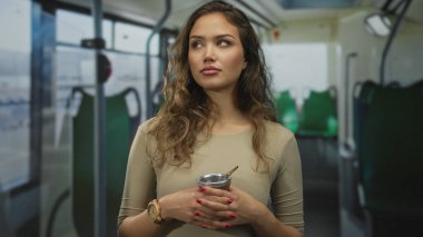 Genç İspanyol kadın, otobüsün içinde bir eş içkisinden zevk alıyor. Elinde bir infüzyon bardağı tutarken, huzurlu bir seyahat deneyimi yakalıyor..